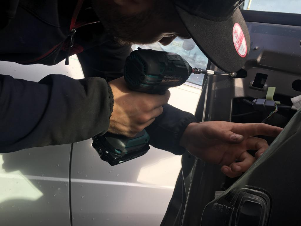 A locksmith from 24/7 Locksmith Solutions in Berkeley using a power drill to work on a vehicle door lock.
