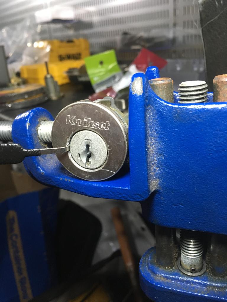 Close-up of a Kwikset lock secured in a blue clamp, highlighting locksmithing tools in a workshop setting.