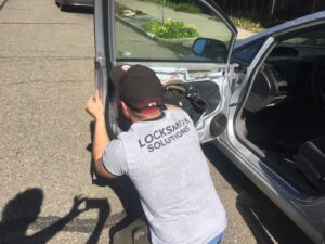 Locksmith in a "Locksmith Solutions" shirt repairing a car door under sunny conditions in Berkeley.