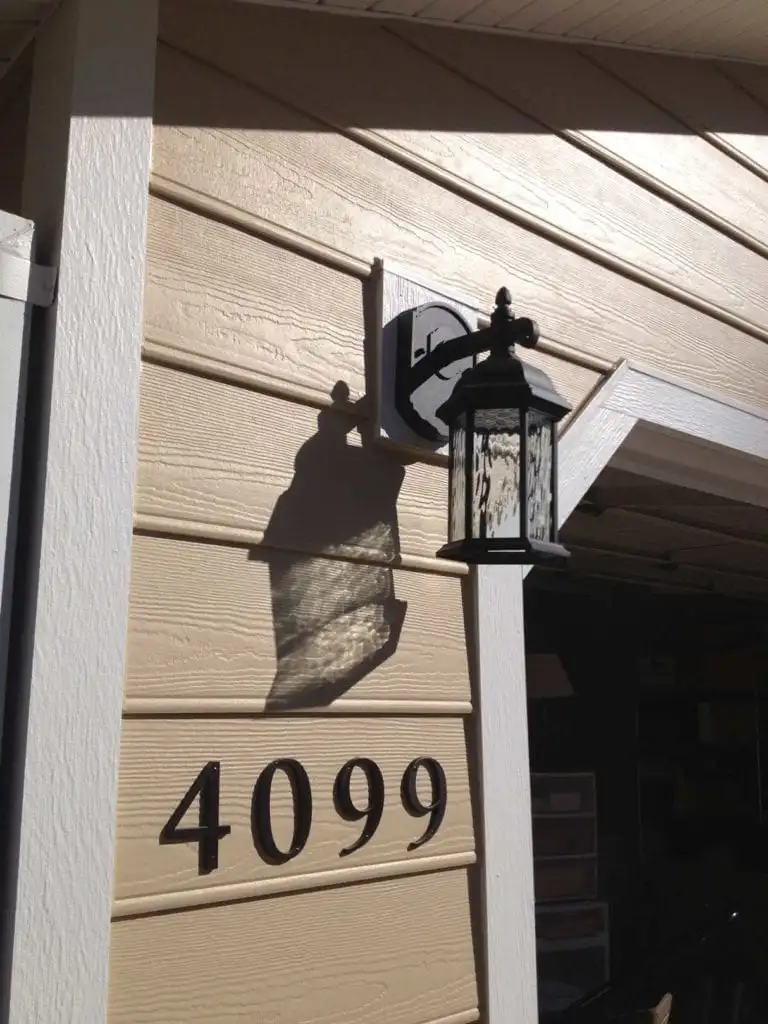 A close-up of a home's entrance with cedar-style shake siding in a warm brown tone, a decorative double door with frosted glass panels, and a black outdoor lantern. Renovation by 3 Generations Improvements, Folsom.