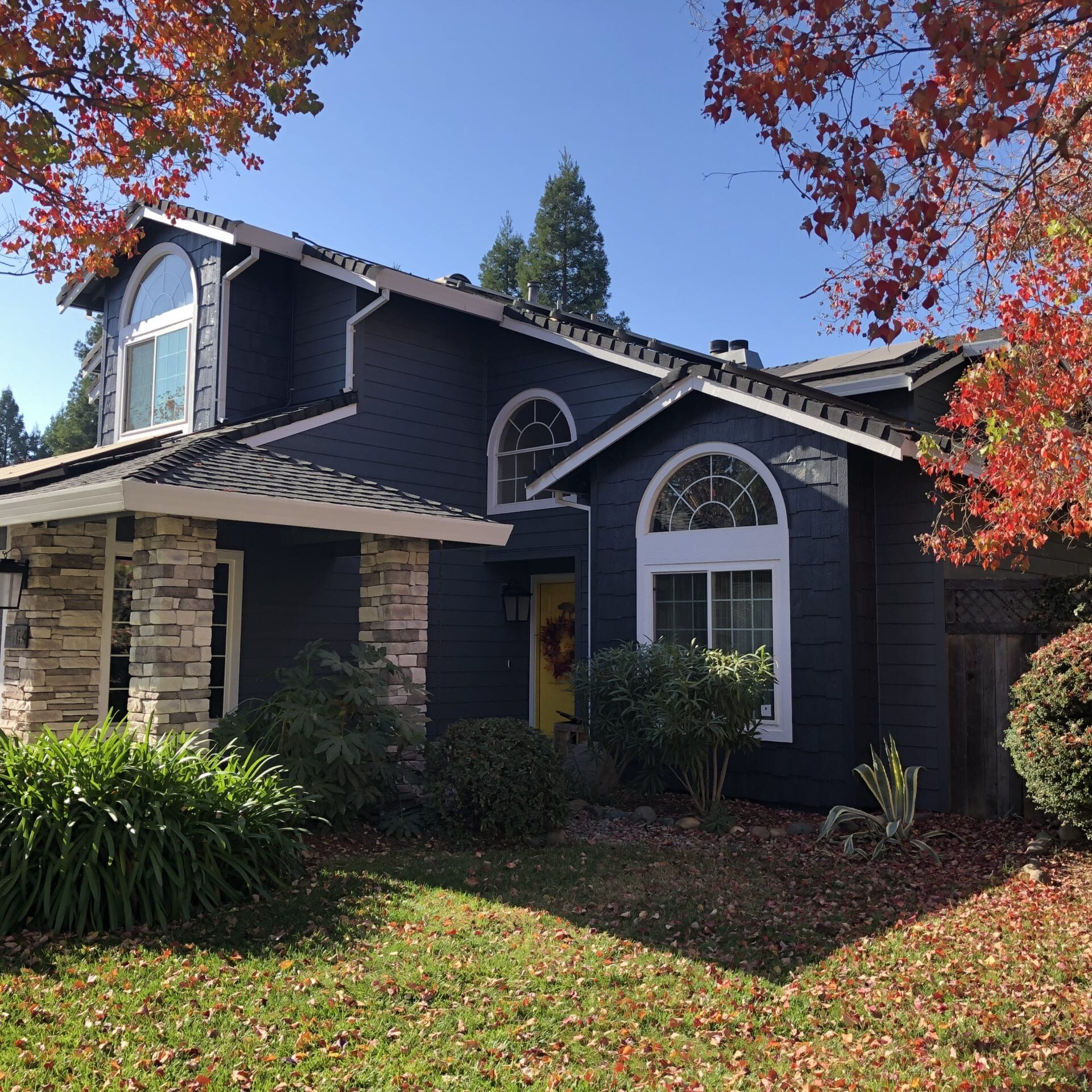 A two-story home in Folsom with dark siding, stone accents, and arched windows, surrounded by autumn foliage.