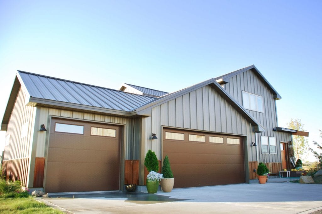 A modern house with a metal roof and large garage doors, enhanced by potted plants and clean landscaping, showcasing 3 Generations Improvements' work in Folsom.