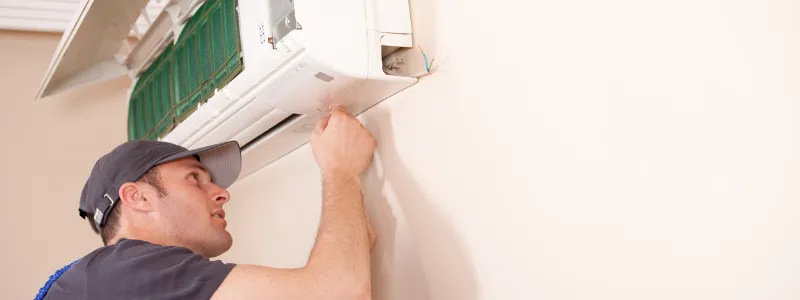 A technician from AIS Heating & Air Conditioning in Livermore performing maintenance on a wall-mounted air conditioning unit.