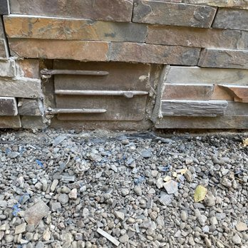 Close-up of a stone wall with metal reinforcement bars and gravel at the base, showcasing ARP Hardscape's craftsmanship in San Leandro.