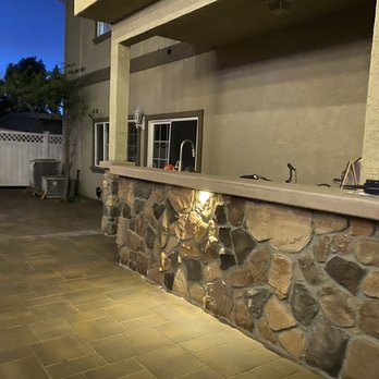 A well-lit stone patio in San Leandro, designed by ARP Hardscape, showcasing a blend of stonework and paving at dusk.