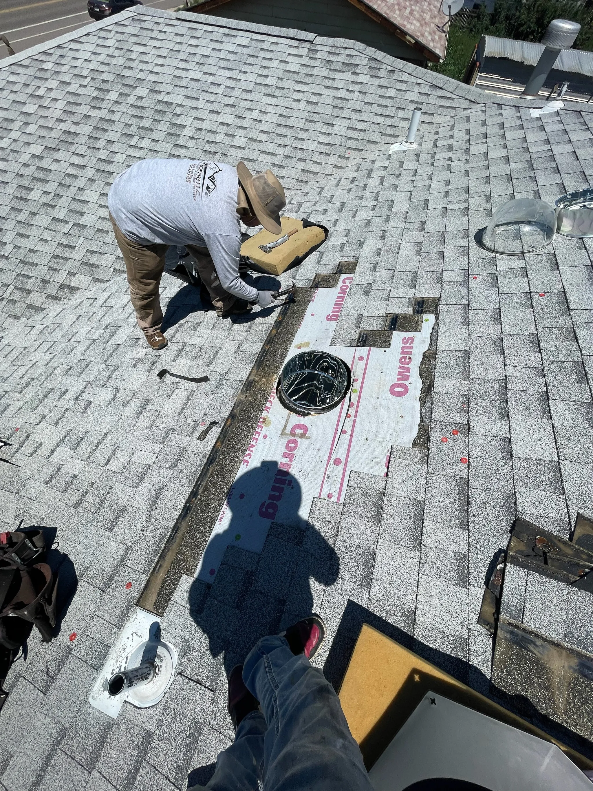 A worker on a roof of gray shingles, installing roofing material with tools and equipment, representing a project by ARS General Contracting LLC in Wheat Ridge.