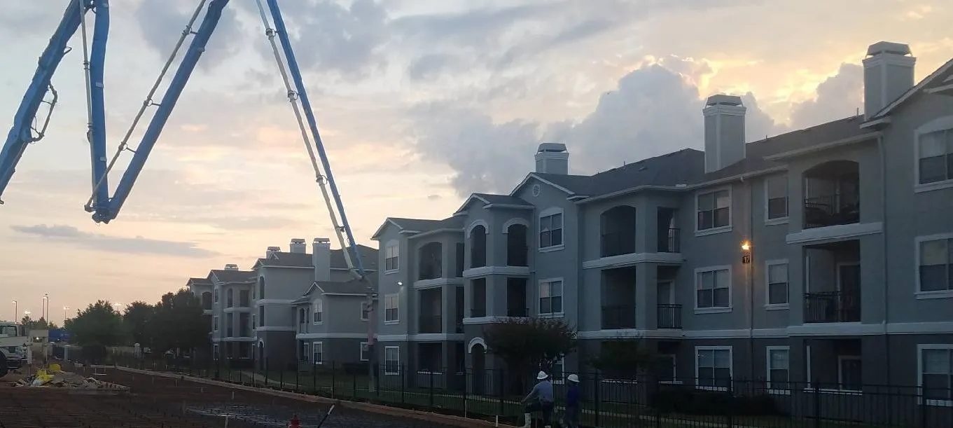 A construction site with a large concrete pump in front of multi-story residential buildings, operated by ARS General Contracting LLC in Wheat Ridge.