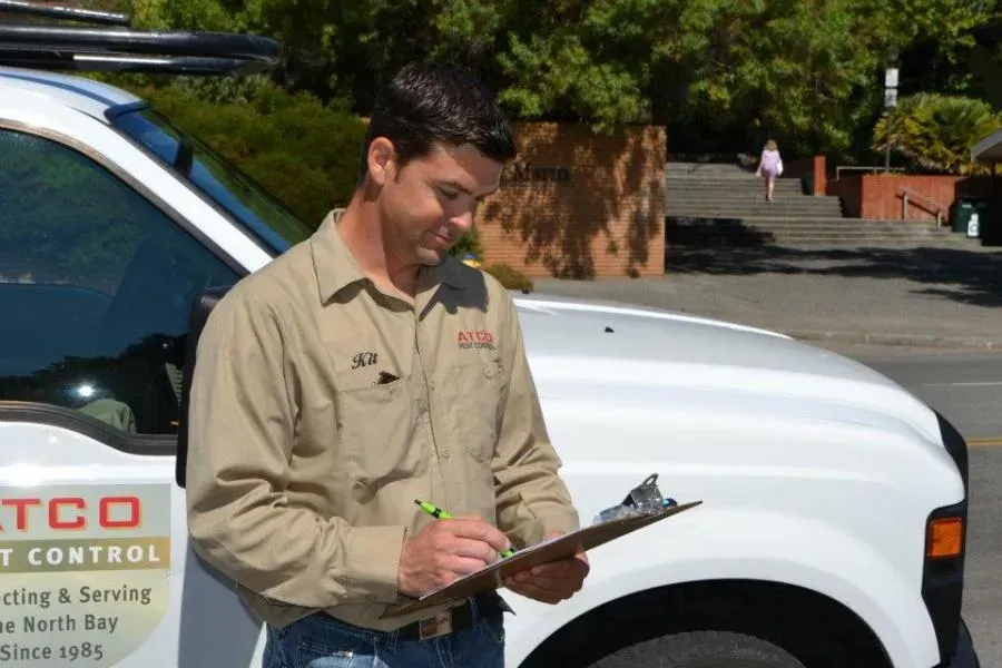 A person from ATCO Pest Control stands next to a company vehicle in Petaluma, writing notes on a clipboard.
