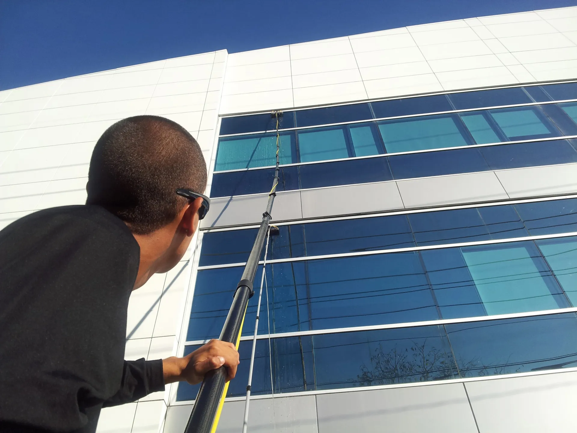 A person cleaning large windows on a modern building using an extended pole, showcasing AWC's window cleaning services in Millbrae.
