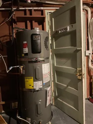 A water heater situated next to an open wooden door in a dimly lit basement.