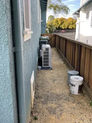 A narrow alley beside a building with an air conditioning unit and two buckets, highlighting the meticulous approach of A-1 Performance Auto Repair in Sunnyvale.