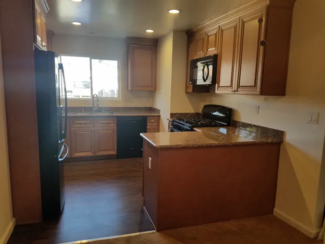 A modern kitchen with wooden cabinets, a granite countertop, a stove, and a window, designed by A Ramos Construction, Inc. in Brentwood.