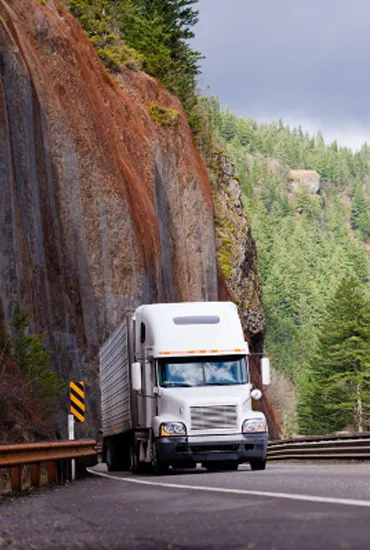 A white truck driving on a scenic highway surrounded by trees and cliffs, representing A and P Moving, Inc. in Novato.