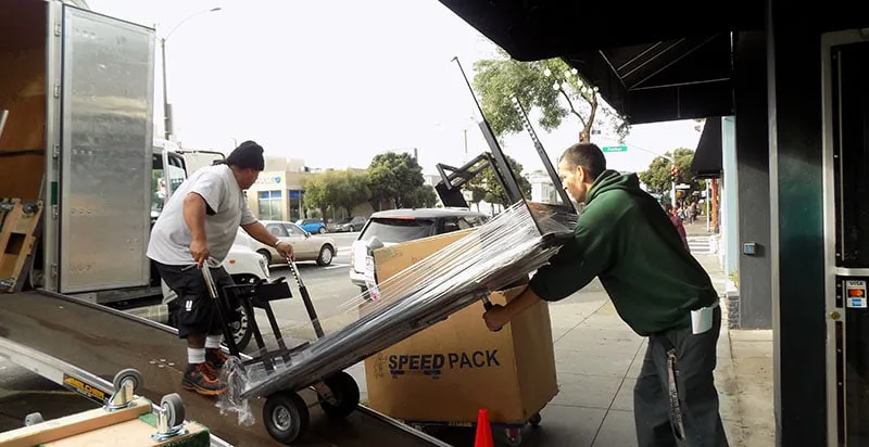 Two movers from A and P Moving, Inc. load a large box onto a truck ramp in Novato, showcasing efficient moving services.