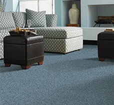A modern living room with patterned sofa, plush blue carpet, and dark brown ottomans, showcasing Abbey Carpets by Fashion Floors in Antioch.