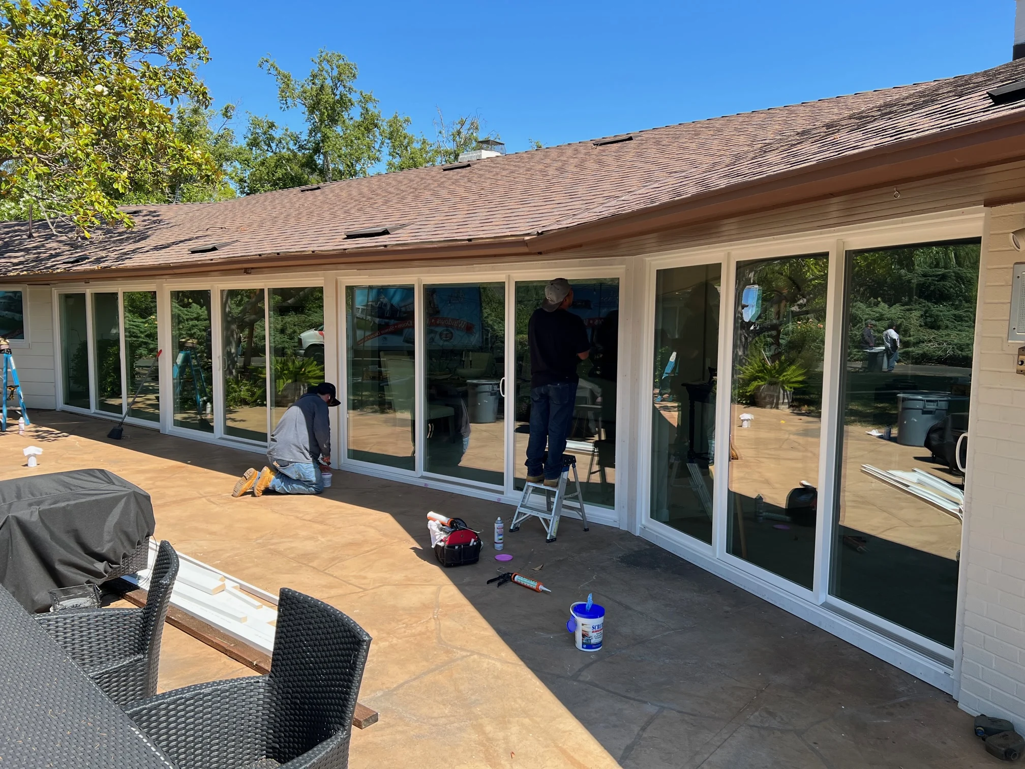 Workers from Able Glass Company installing large glass panels on a patio in Santa Clara, surrounded by tools and outdoor furniture.