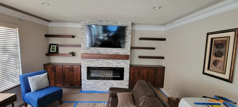 A modern living room in Pleasanton featuring a stone fireplace with a mounted TV, surrounded by wooden shelves and cabinetry, showcasing the work of Abrew Repair and Construction.