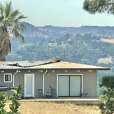A house with a flat roof under renovation, surrounded by hills and greenery in Martinez, serviced by Abril Roofing, Inc.