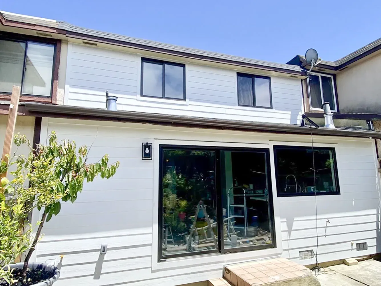 "A renovated white two-story house featuring large, modern windows and sliding glass doors, enhanced by Abstract Windows in San Carlos."