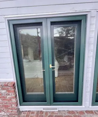 A pair of green-framed glass doors installed on a brick and siding wall, showcasing Abstract Windows' design in San Carlos.
