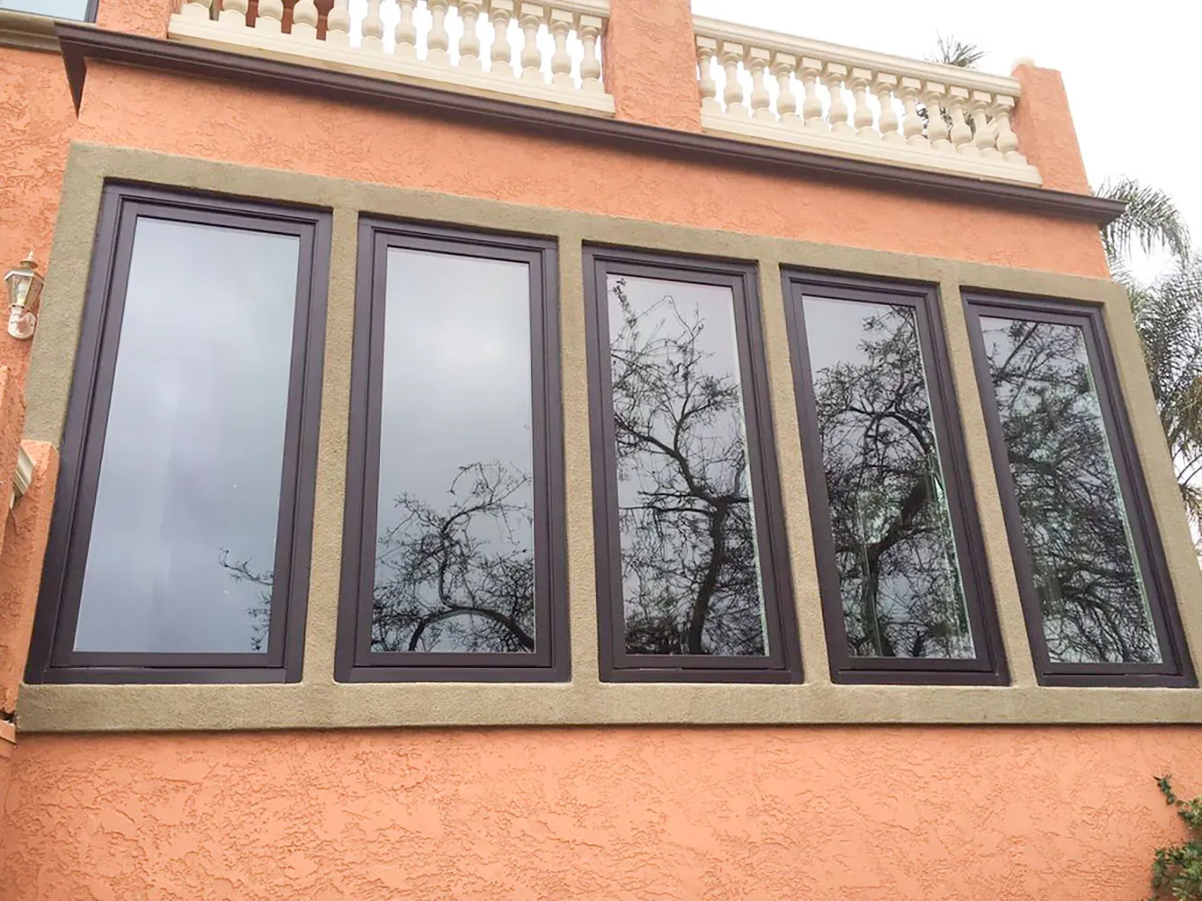 A row of five large, reflective windows with dark frames set in a peach-colored wall, surrounded by beige trim.