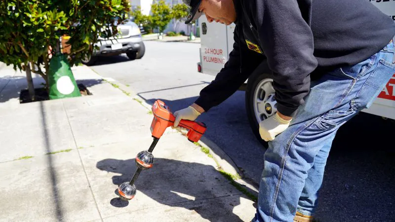 A technician from Ace Plumbing and Rooter in San Francisco uses a leak detection device on a sidewalk to locate underground plumbing issues.