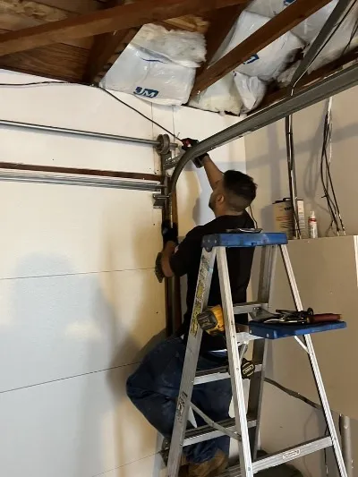 "A technician from Ace's Garage Door Repair & Installation in Hayward working on a garage door mechanism using a ladder and tools."
