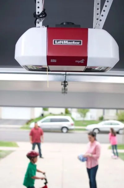 A garage door opener hanging in focus, with a family in the background outside, illustrating a residential setting.