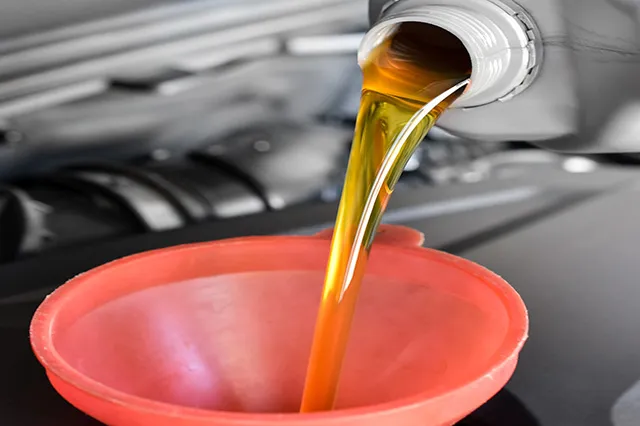 Close-up of oil being poured into a car engine through a red funnel, representing a service offered by Acur-It Auto Repair in Rohnert Park.