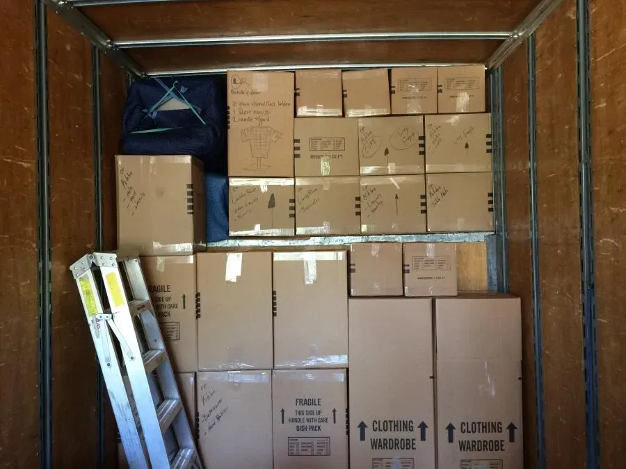 Interior of a moving truck filled with neatly stacked and labeled cardboard boxes, with a ladder on the left side.