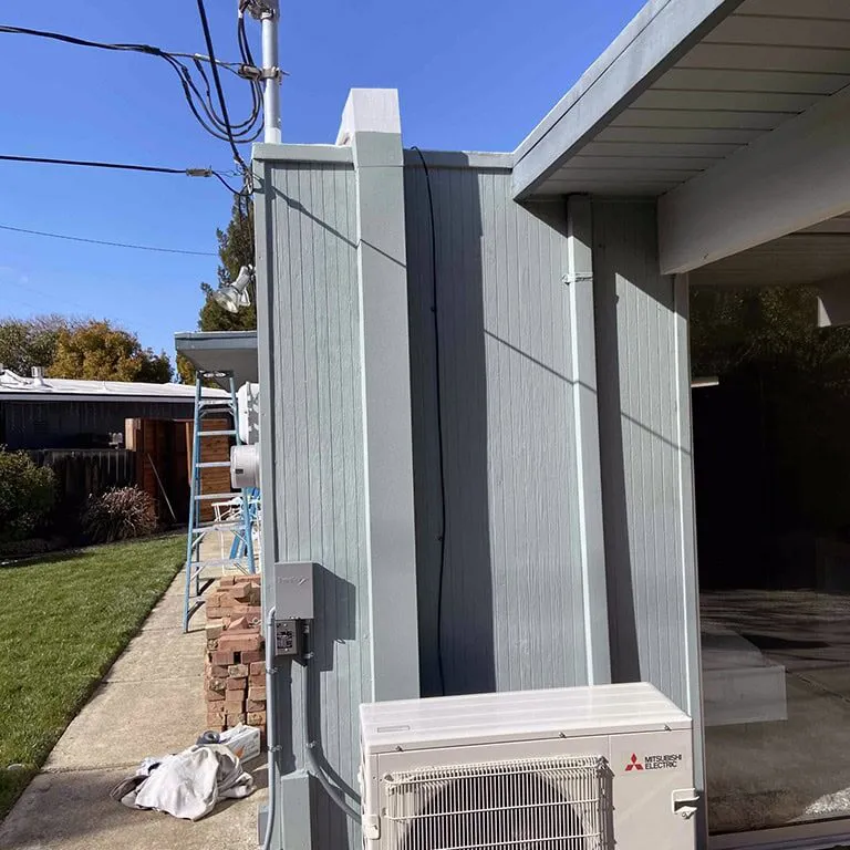 An outdoor air conditioning unit installed on the exterior wall of a house, surrounded by a green lawn and clear blue sky, showcasing Air Care Heating & Cooling, Inc.'s work in San Jose.