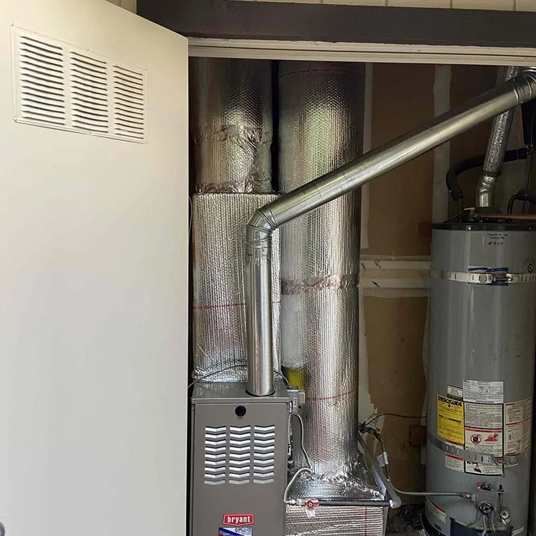 A furnace and water heater installed in a utility closet, showcasing insulated pipes and ducts designed for efficient heating by Air Care Heating & Cooling, Inc. in San Jose.