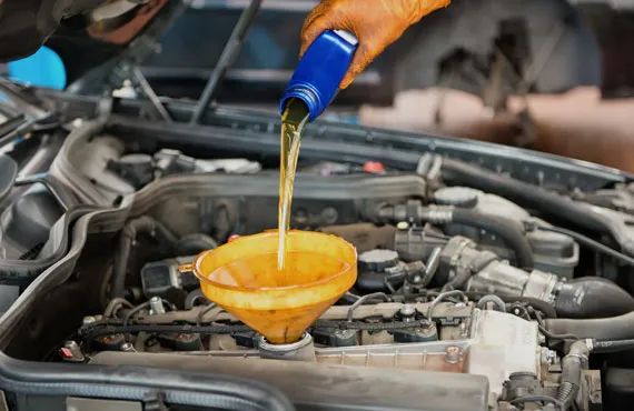 A gloved hand is pouring motor oil into a car engine using a funnel, depicting an oil change service.