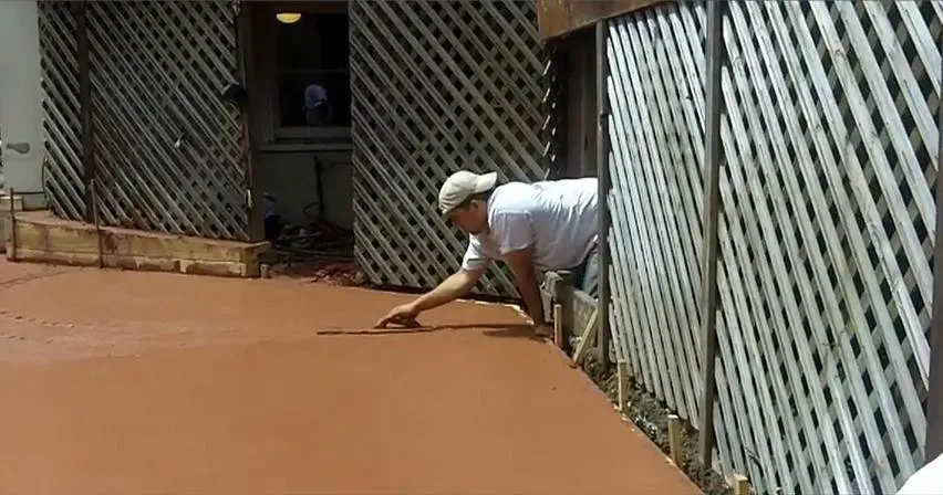 A person from All Seasons Construction smoothing wet concrete next to lattice fencing in Oakland.