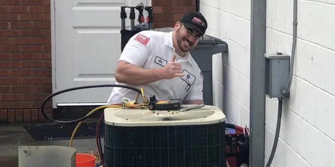 A technician from All Weather Heating & Air Conditioning Inc. in Vacaville is smiling and giving a thumbs-up while servicing an outdoor air conditioning unit.
