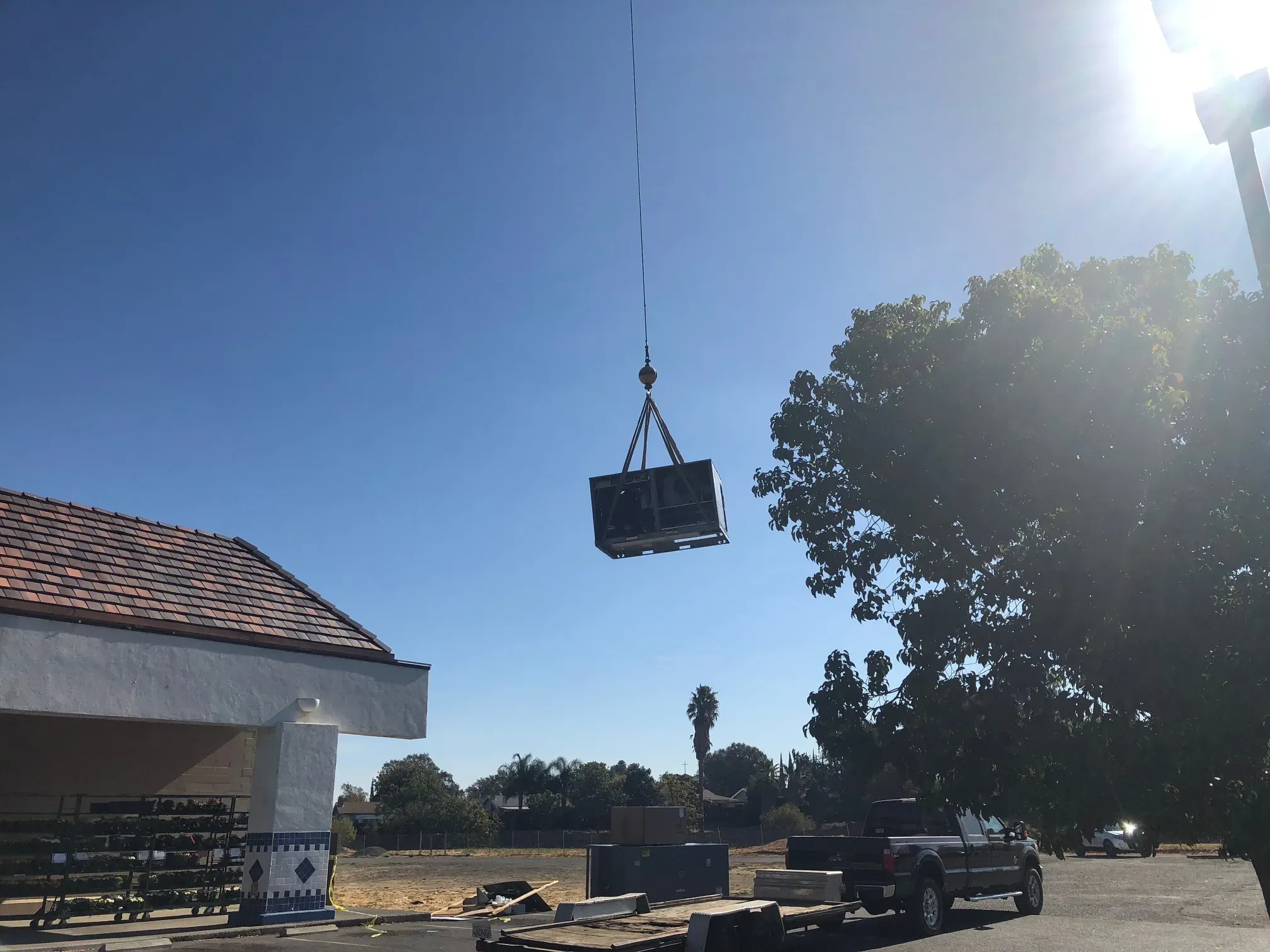 An HVAC unit being installed using a crane outside a building on a sunny day in Vacaville, with a tree and a truck nearby.