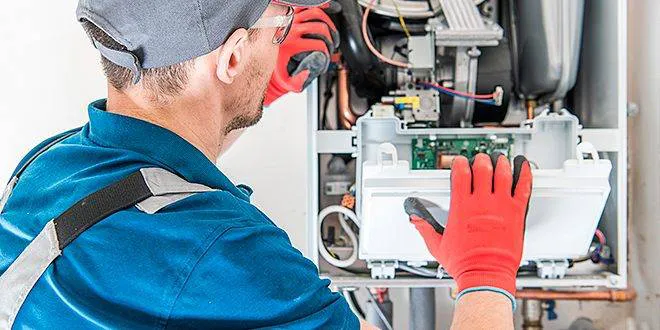 Technician wearing red gloves and a blue uniform servicing a heating unit, embodying the efficient service provided by All Weather Heating & Air Conditioning Inc. in Vacaville.