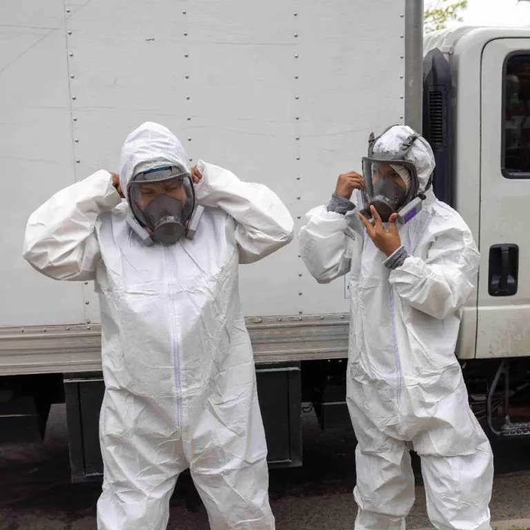 Two people in protective suits and masks standing next to a truck, preparing for a task.