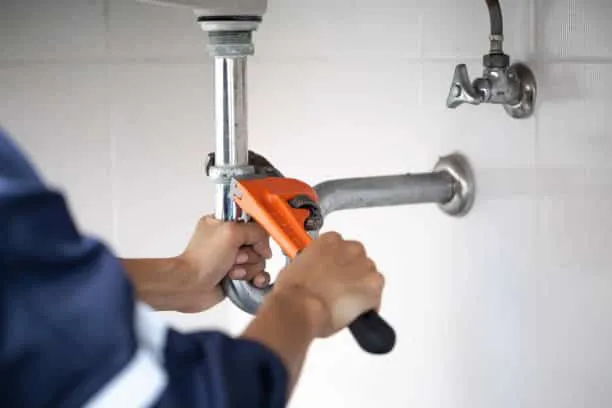 Plumber using a wrench to fix a pipe under a sink.