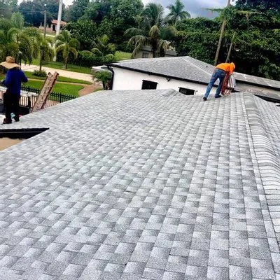 "Two workers on a newly shingled roof, with lush greenery in the background, demonstrating Alonso Roofing's craftsmanship in Hialeah."