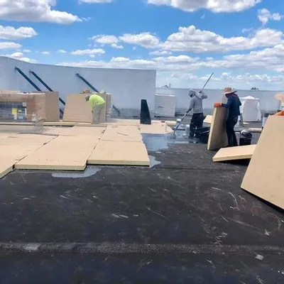Workers installing roofing materials on a flat roof under a blue sky with clouds, representing Alonso Roofing in Hialeah.