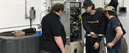 A group of technicians examining and discussing an HVAC system at Alternative Heating & Air Conditioning Solutions, Inc. in San Carlos.