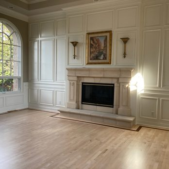 A spacious room with light hardwood flooring, a large arched window, and a sophisticated fireplace, showcasing the craftsmanship of Alva Flooring Inc. in Oakland.
