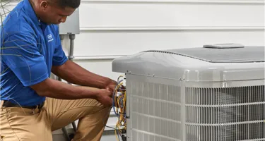 A technician wearing a blue shirt works on an outdoor HVAC unit next to a building in South San Francisco.