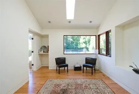 A bright, minimalist room with two black chairs, a rug, large windows, and wooden flooring, designed by An Ky Construction Inc. in San Jose.