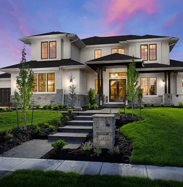 A modern, two-story house with large windows and a well-manicured lawn during sunset.