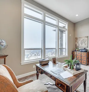 A bright home office with a large window installed, allowing ample natural light to fill the room, featuring elegant furniture and decor.