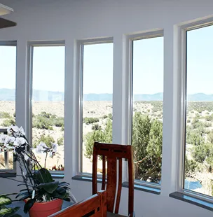 A series of large windows installed in a home, offering a view of a scenic landscape with trees and hills, enhanced by natural light.