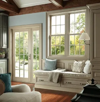 A cozy living room with large windows and a glass door installed by Anderson Window & Door Installation, featuring a built-in bench with cushions and a view of a garden outside.