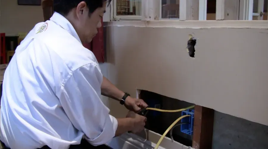 A technician from Aren Electric Co., Inc. works on installing electrical wiring through a wall in Daly City.